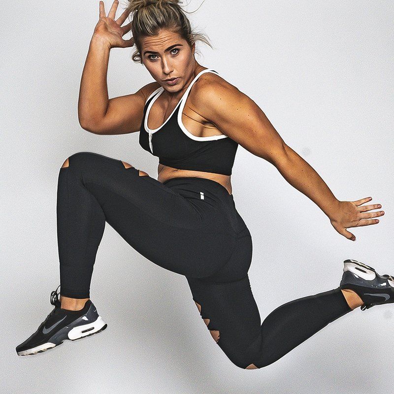 A woman in a black sports bra and black leggings is jumping in the air