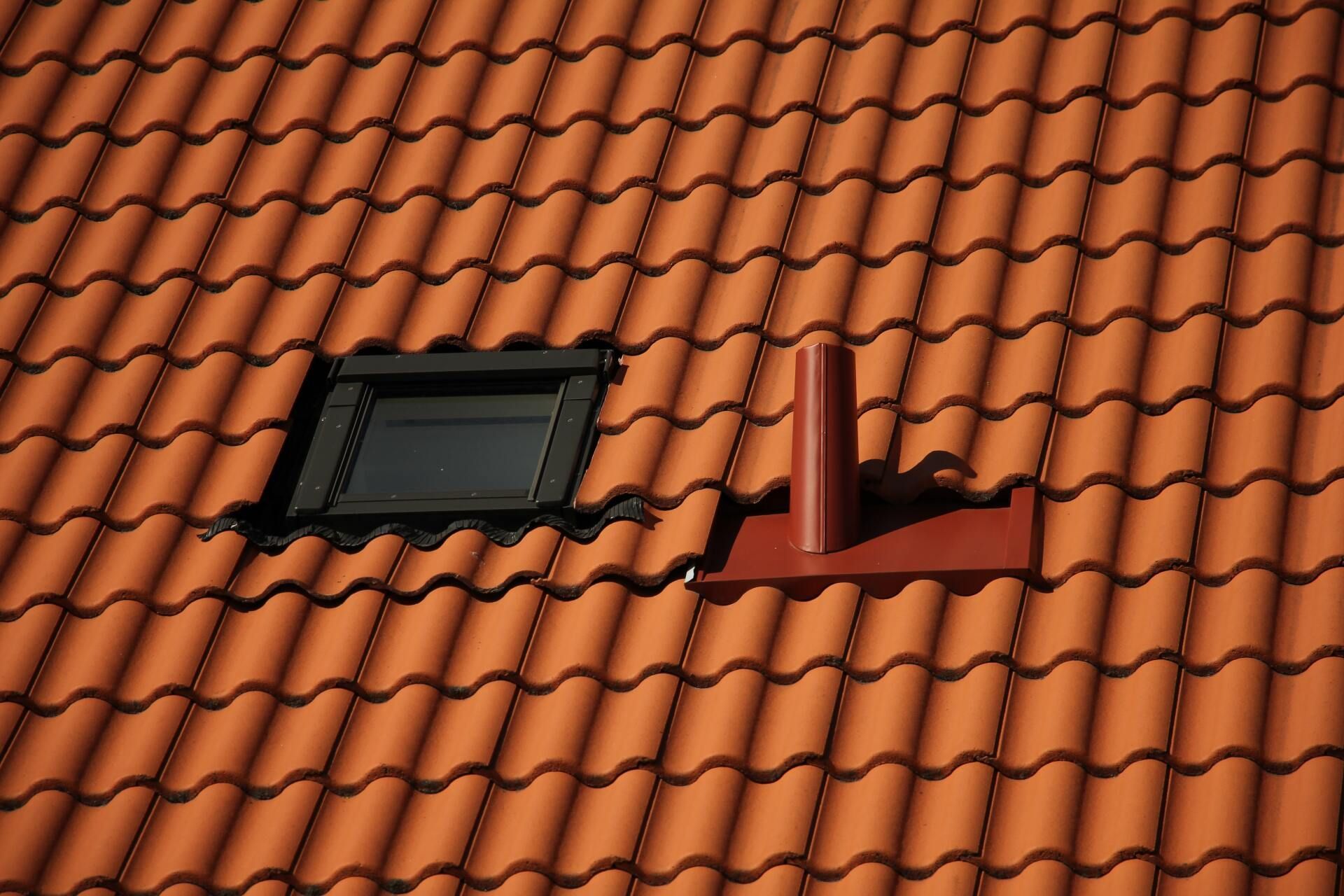 Red tiled roof with a dark-framed skylight and a red ventilation pipe.