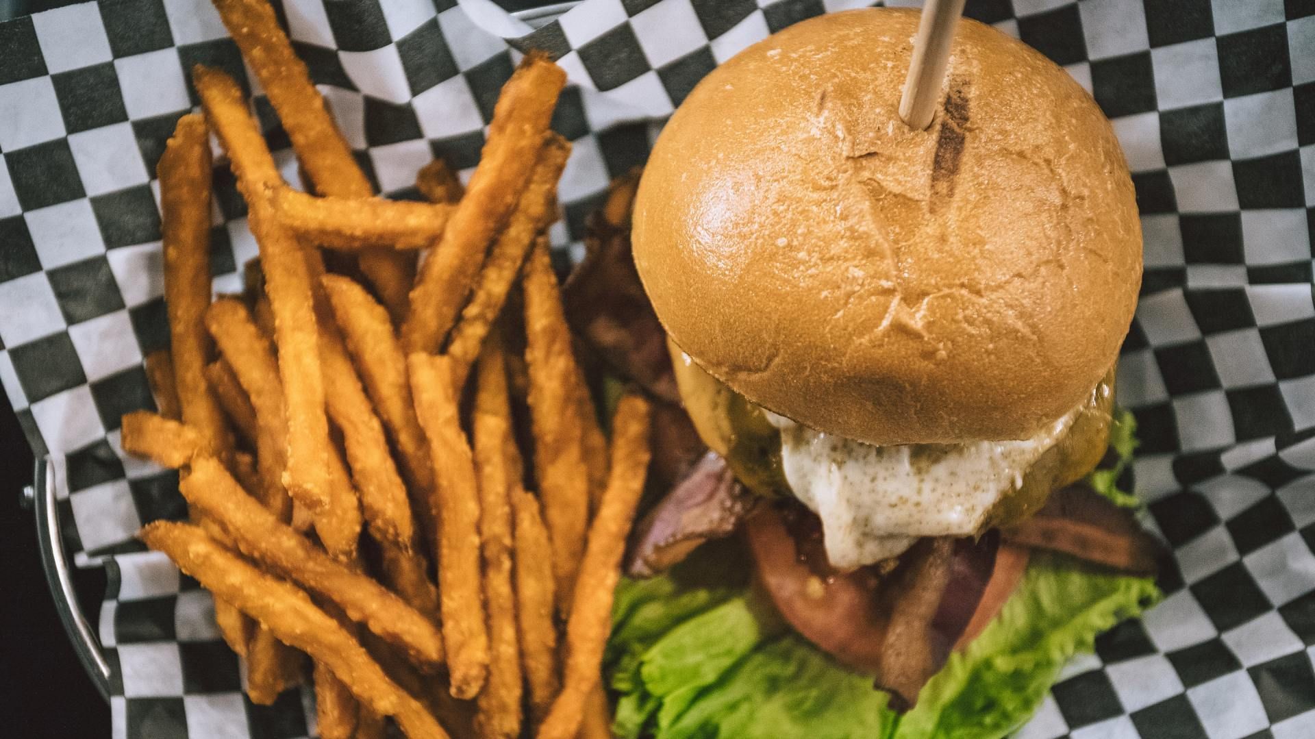 A hamburger and french fries in a basket on a checkered paper.