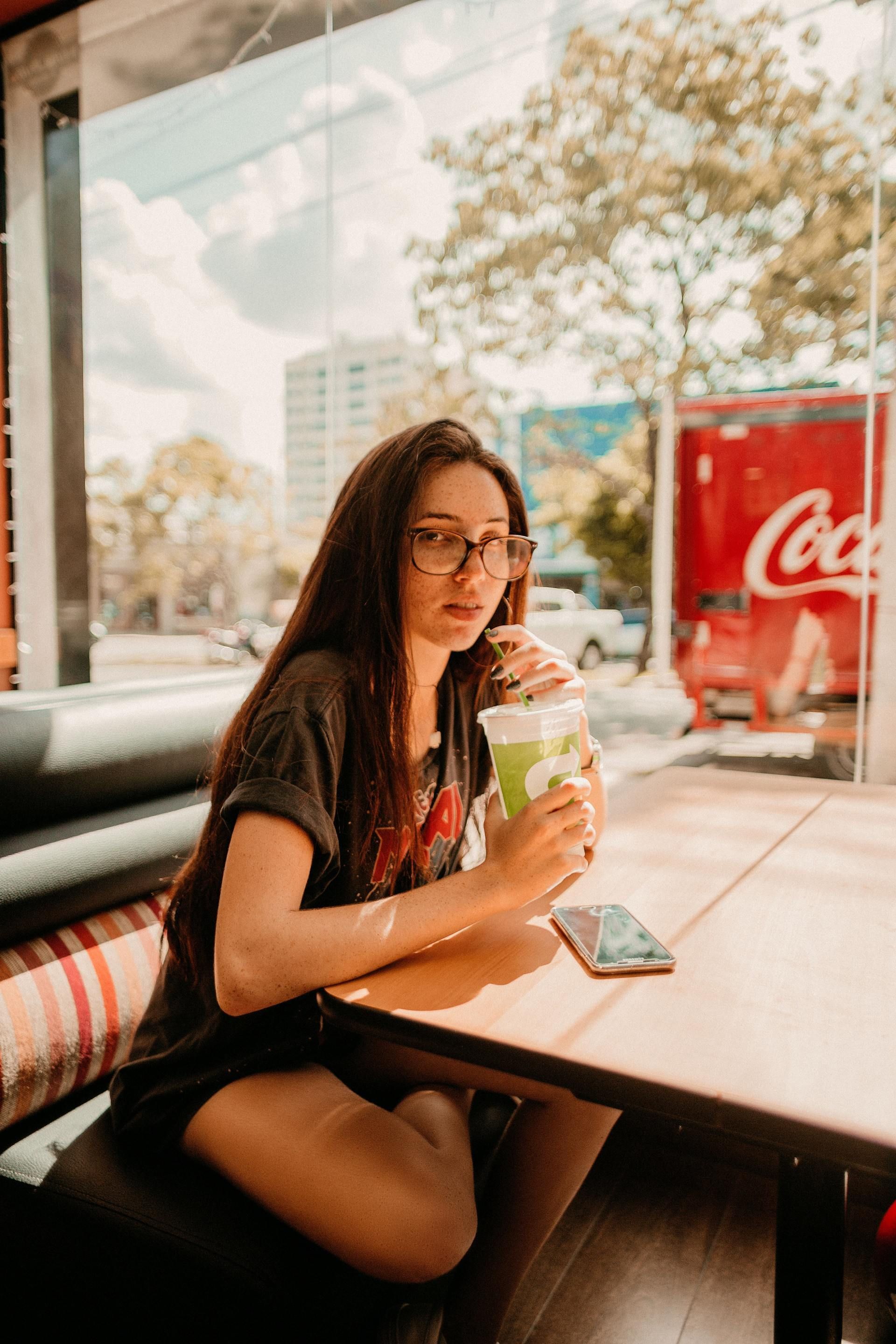 A woman is sitting at a table drinking a green drink.