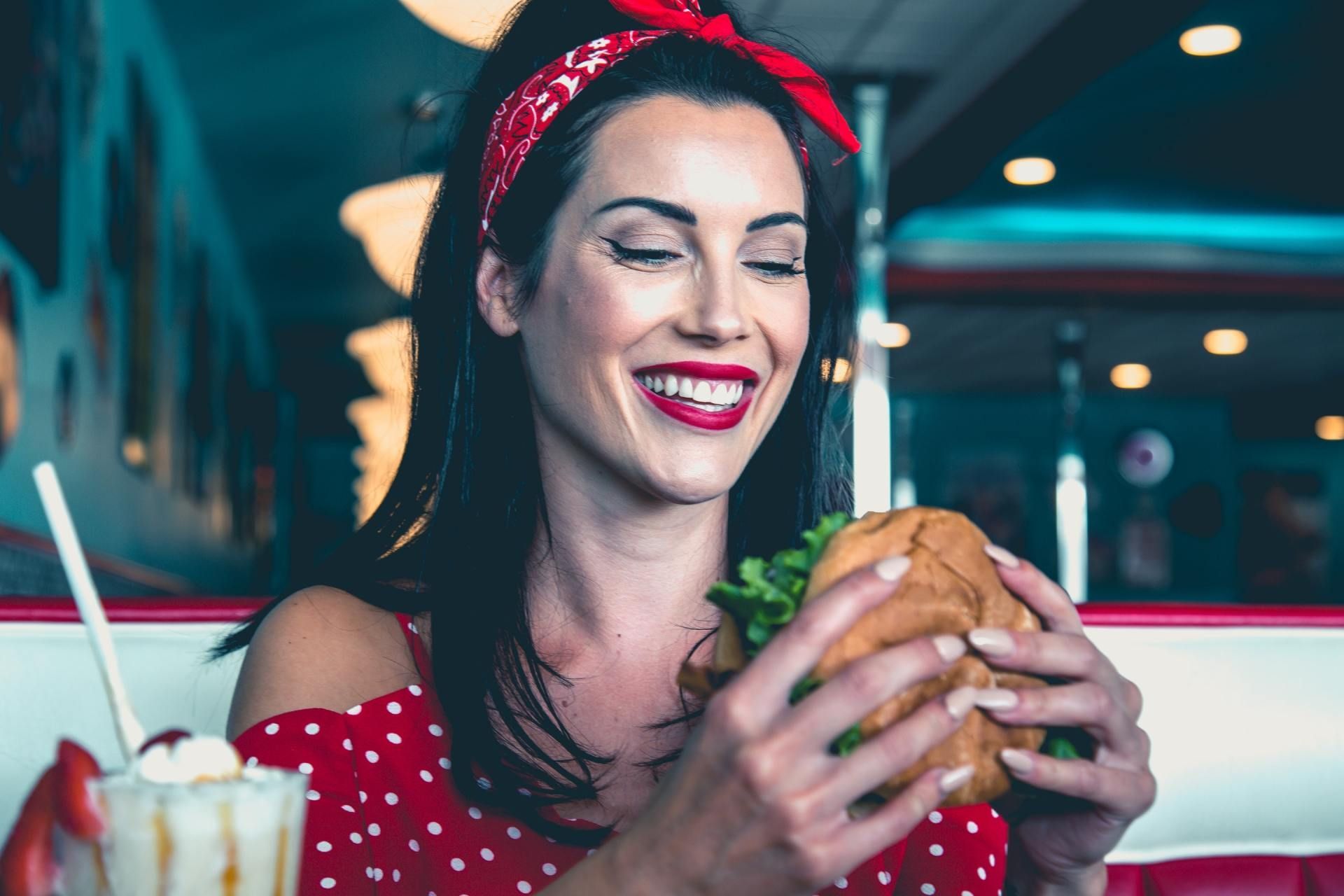 A woman is eating a hamburger in a diner and smiling.