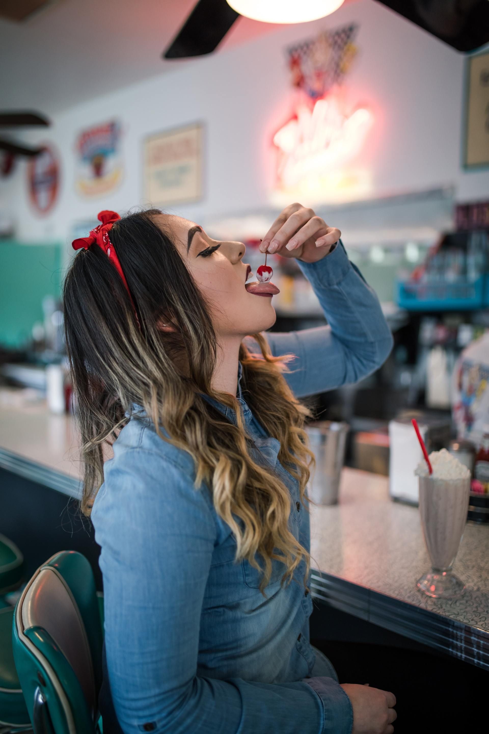 A woman is sitting at a diner eating a cherry.