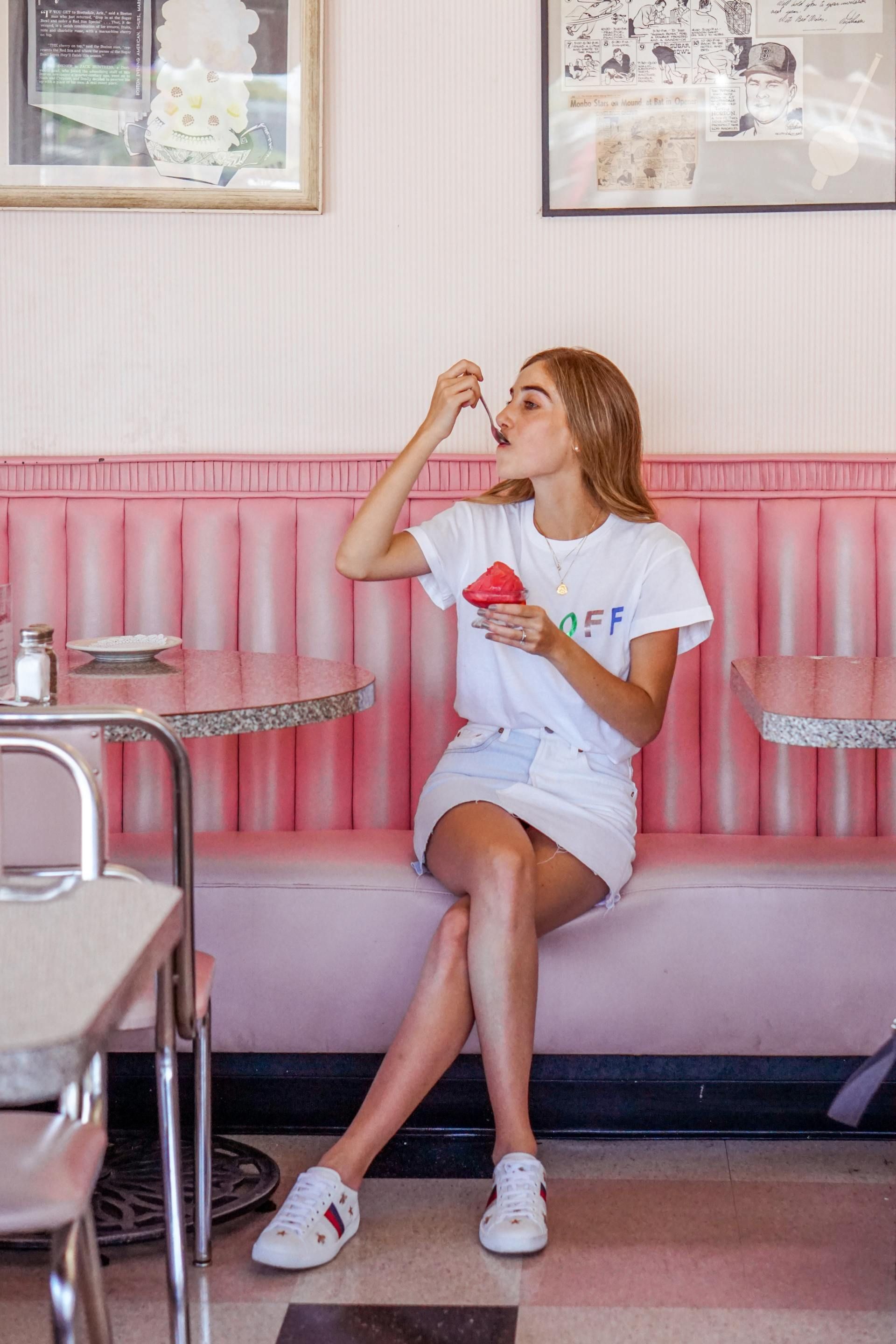 A woman is sitting on a pink couch eating ice cream.