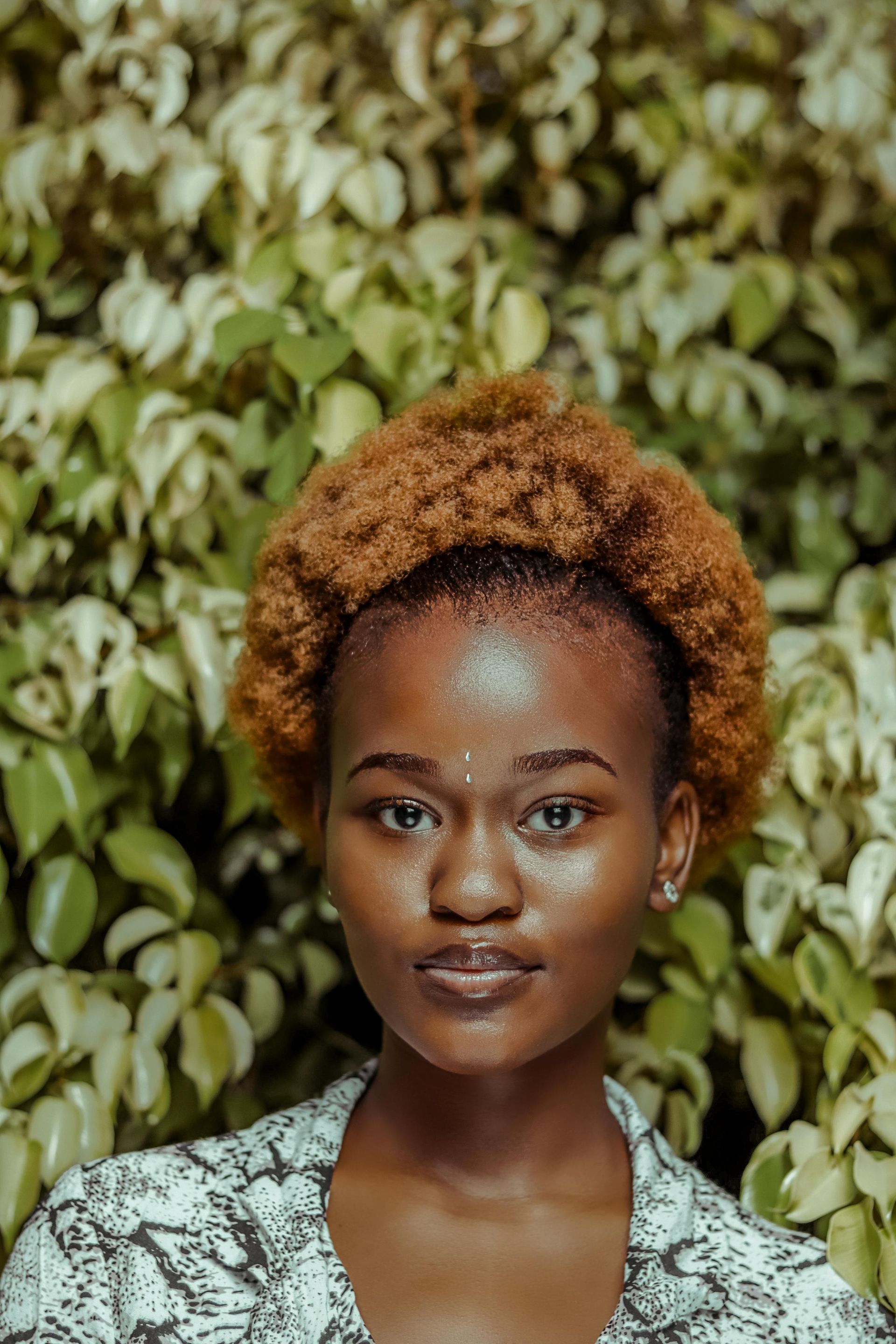 A woman with curly hair is standing in front of a bush.