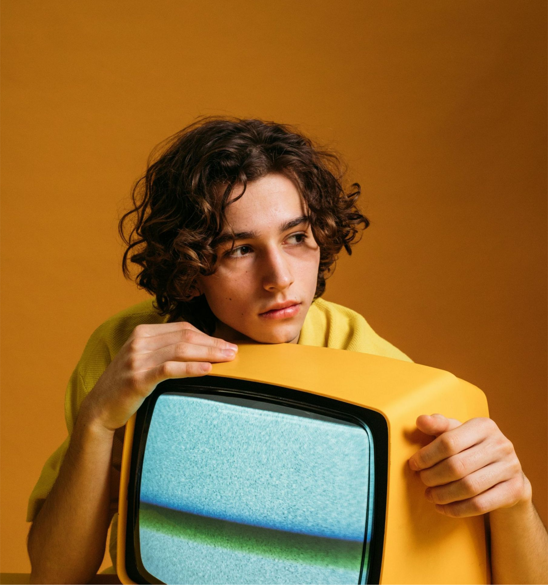 A young man is holding a yellow television in his hands.