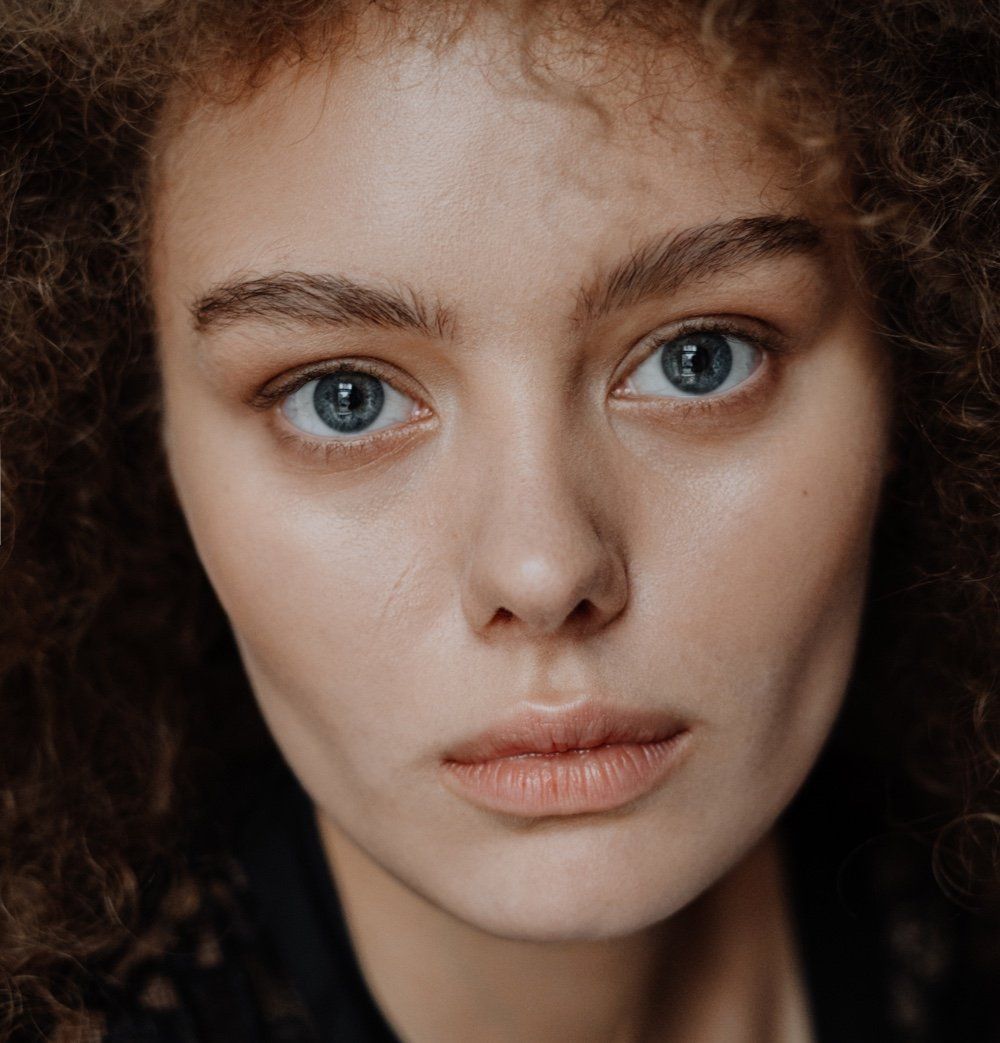 A close up of a woman 's face with curly hair and blue eyes