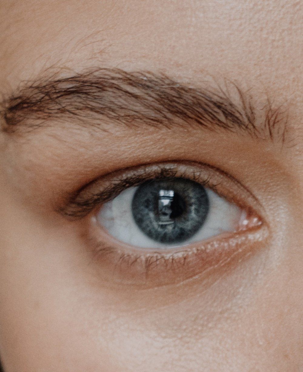 A close up of a woman 's blue eye with brown eyebrows.