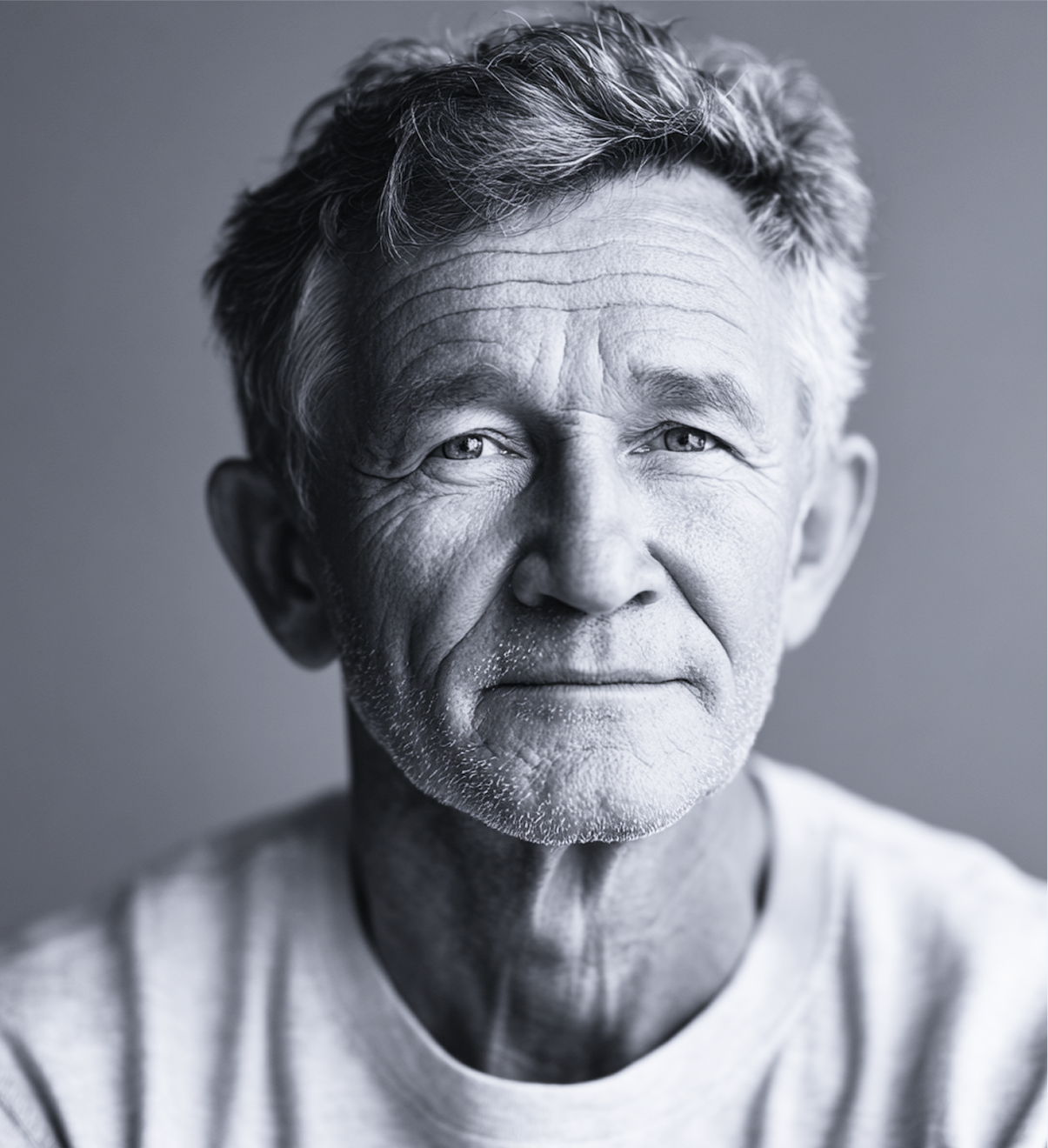 A close-up, black and white portrait of an older man with a neutral expression, wearing a white shirt.