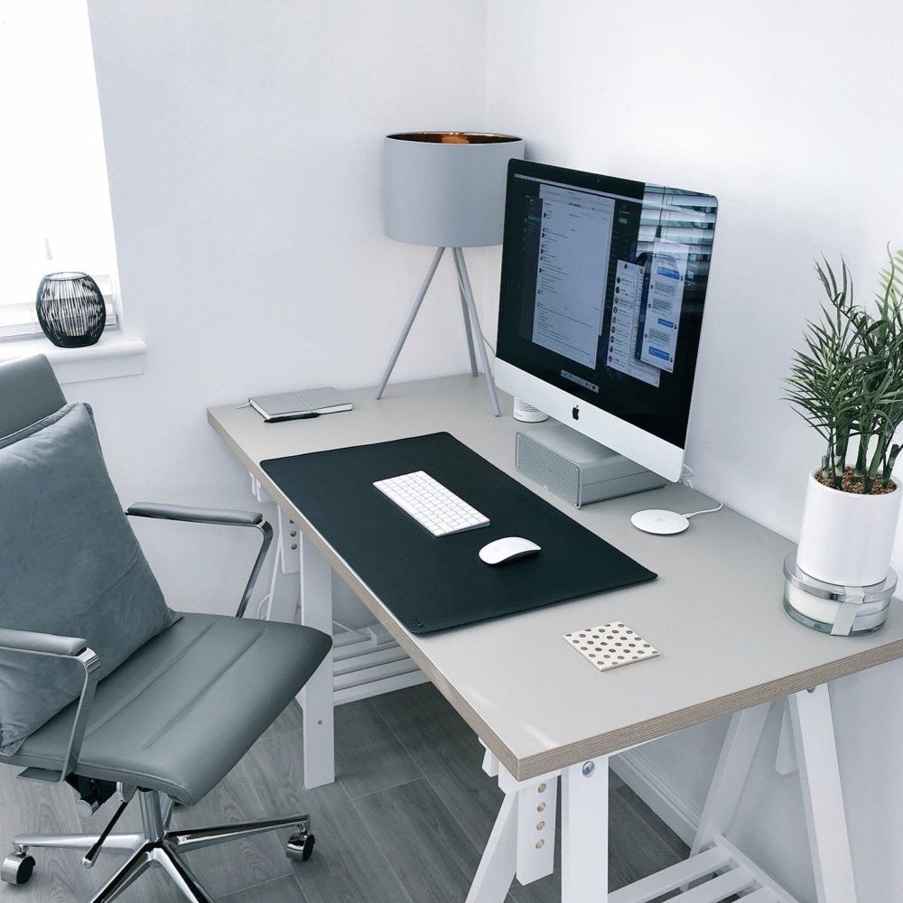 Un moderno ufficio domestico con un computer, una lampada, una pianta in vaso e una sedia da ufficio grigia.