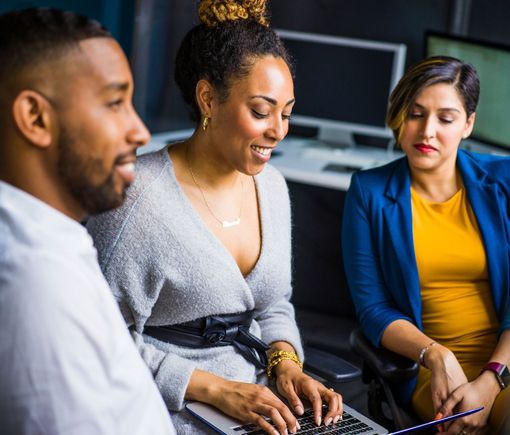 A group of people are sitting around a laptop computer.