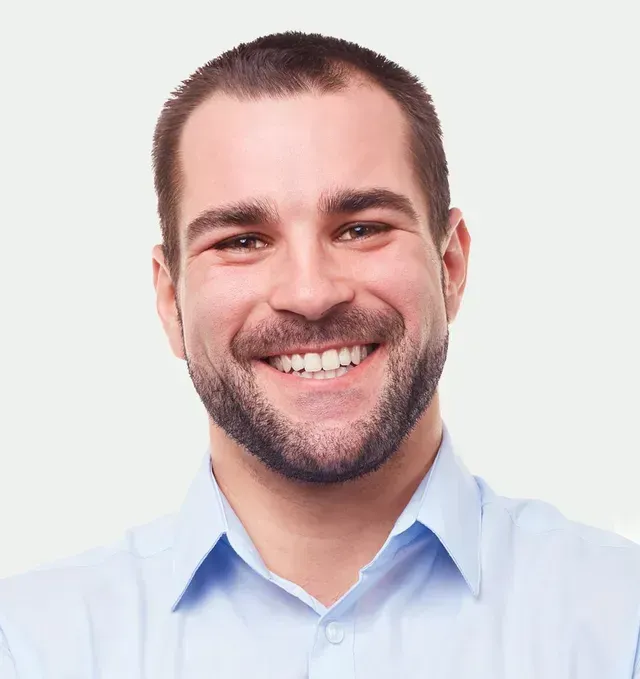 A man with a beard is smiling and wearing a blue shirt.