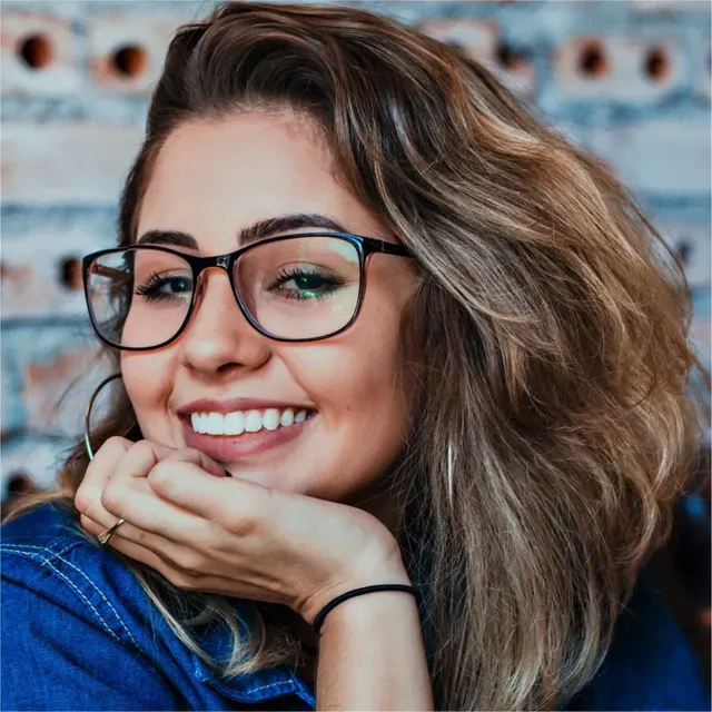 Une femme portant des lunettes sourit avec sa main sur son menton.