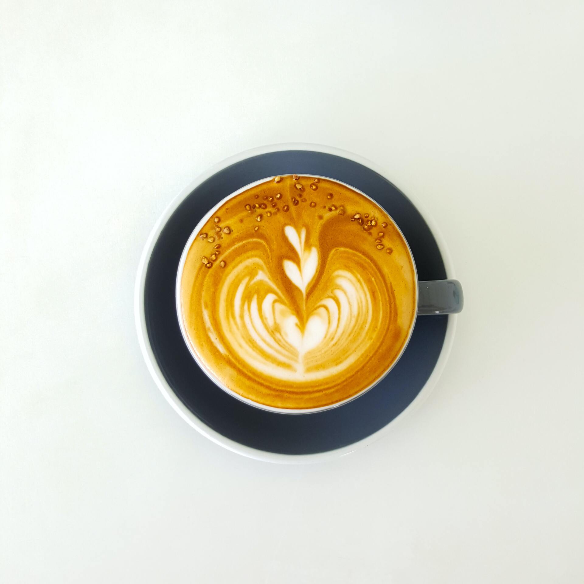 Latte in een donkerblauwe kop en schotel, met latte art.