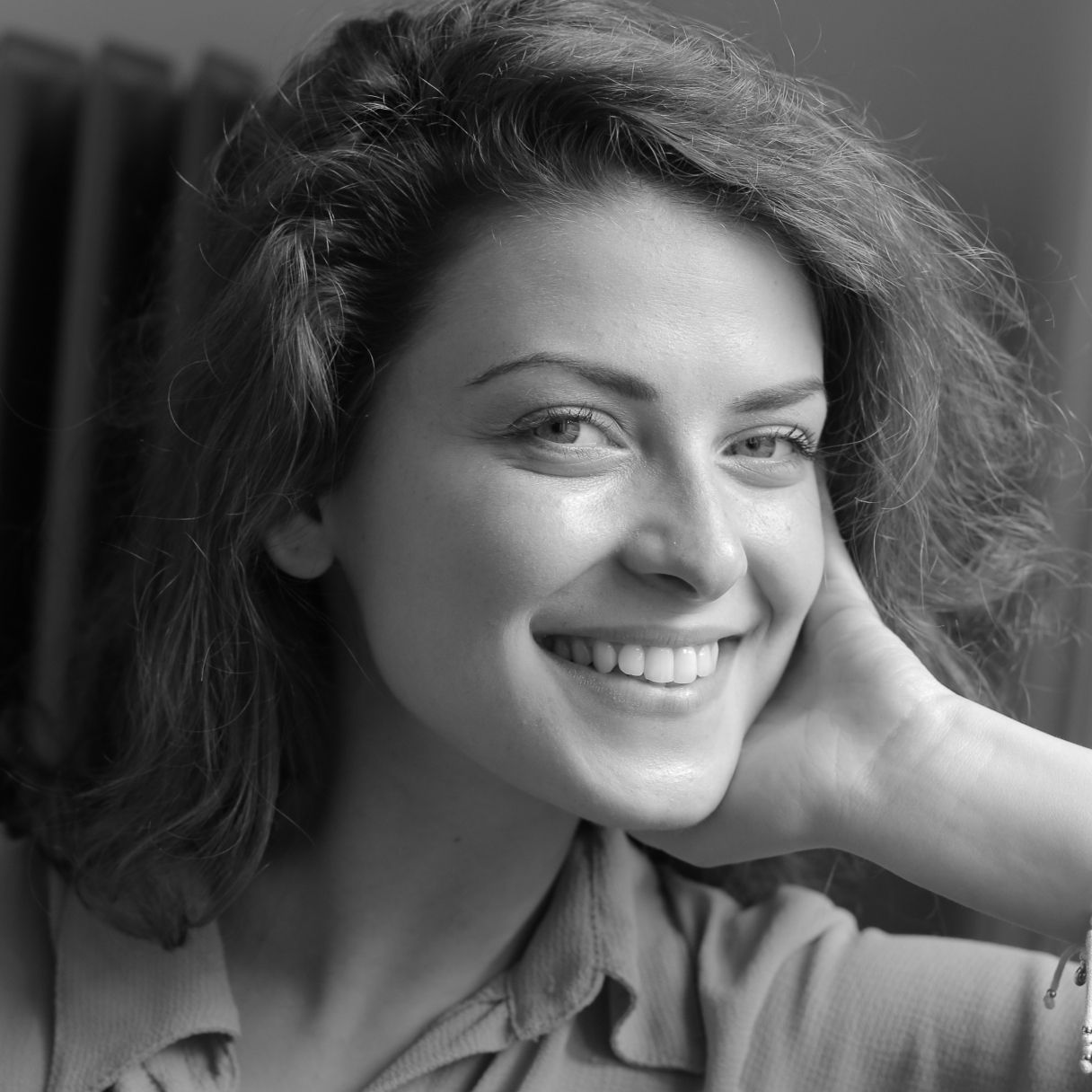 A black-and-white portrait of a smiling person resting their chin on their hand.