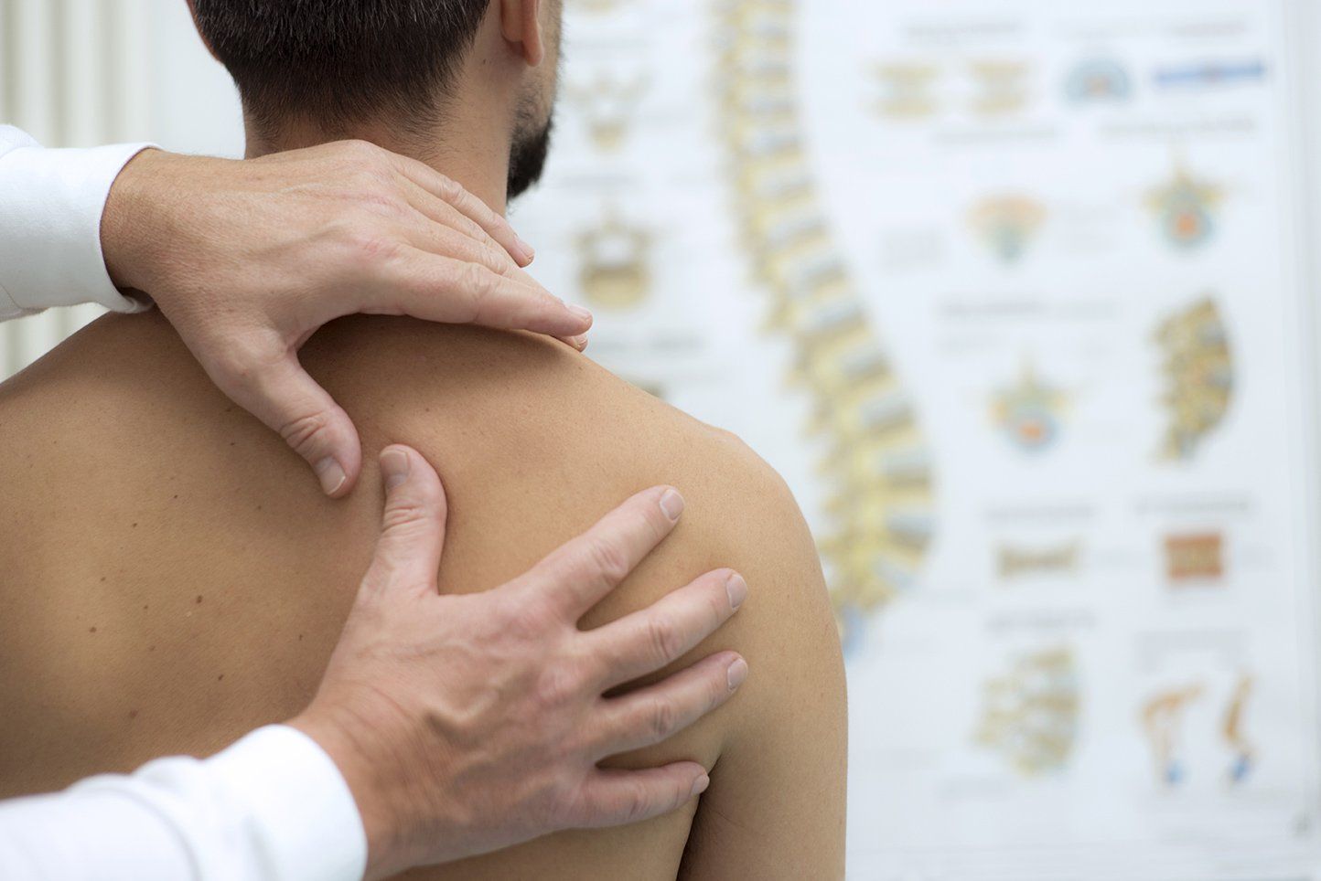 Hands examine a person's shoulder. A spinal chart is in the background.