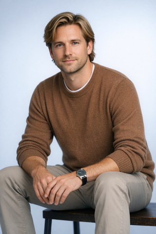 Seated man in a brown sweater and light pants, posing against a plain light background.