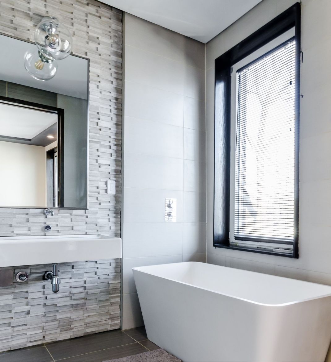 Salle de bain moderne avec une baignoire blanche autoportante, une fenêtre avec stores et un mur à texture de pierre.
