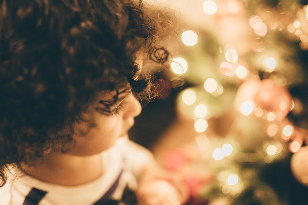 A little girl with curly hair is looking at a christmas tree.