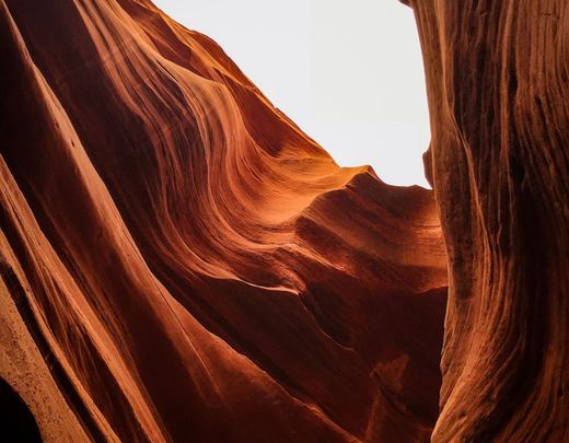 Sunlit red sandstone canyon with flowing ridges and a bright sky opening above