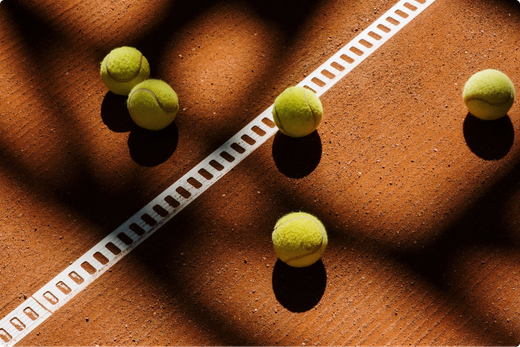 Several tennis balls on a clay court beside a white line, with long shadows.
