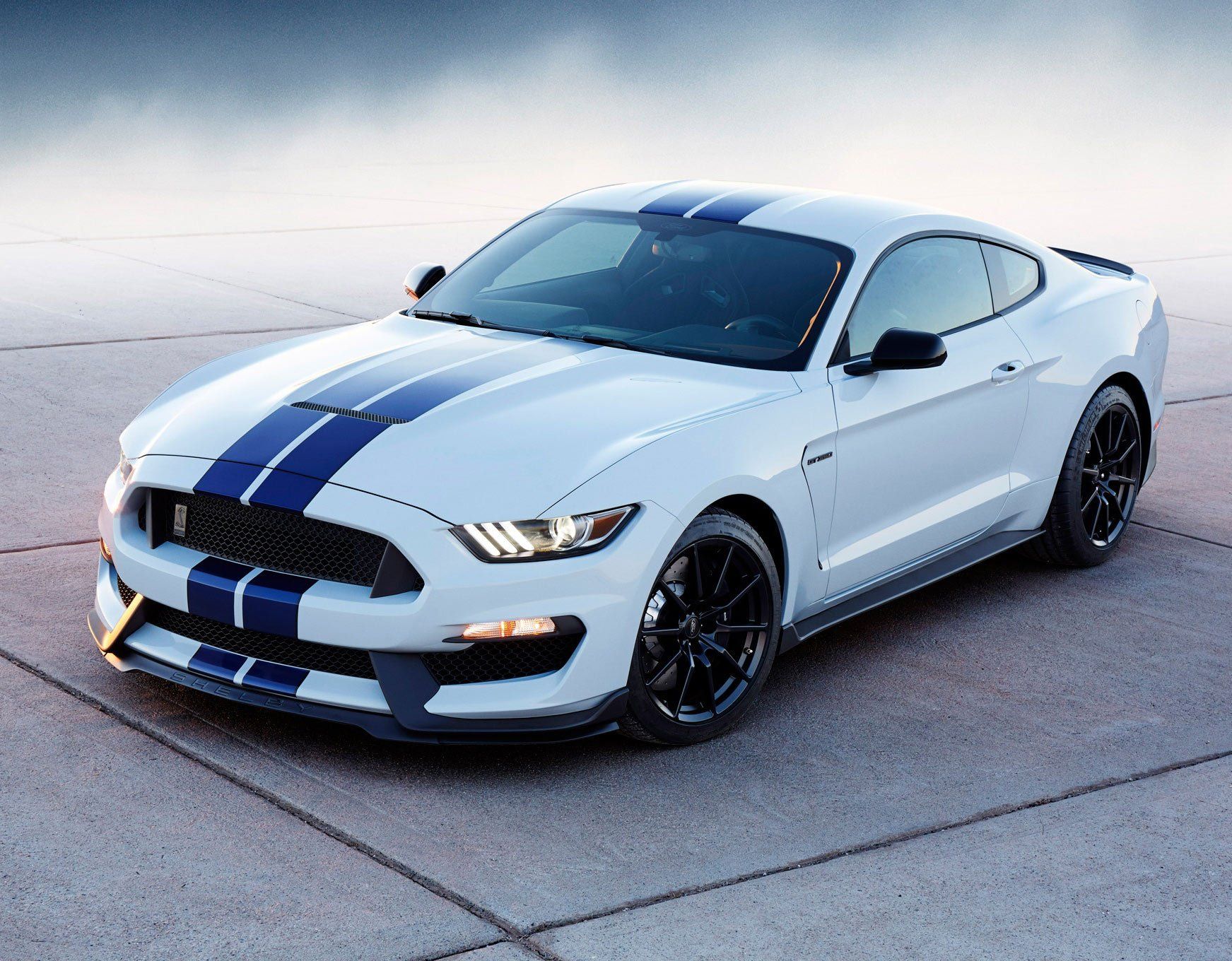 A white ford mustang with blue stripes is parked on the side of the road.
