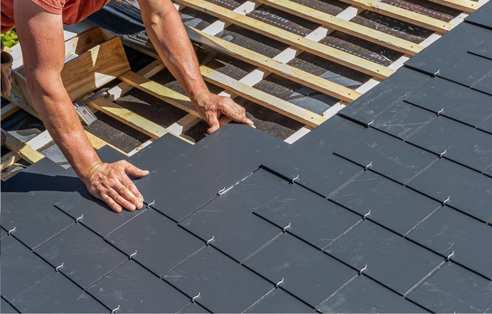 A man is working on a roof with slate tiles.