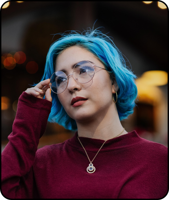 Woman with blue hair, round glasses, and a maroon top. She looks away thoughtfully.