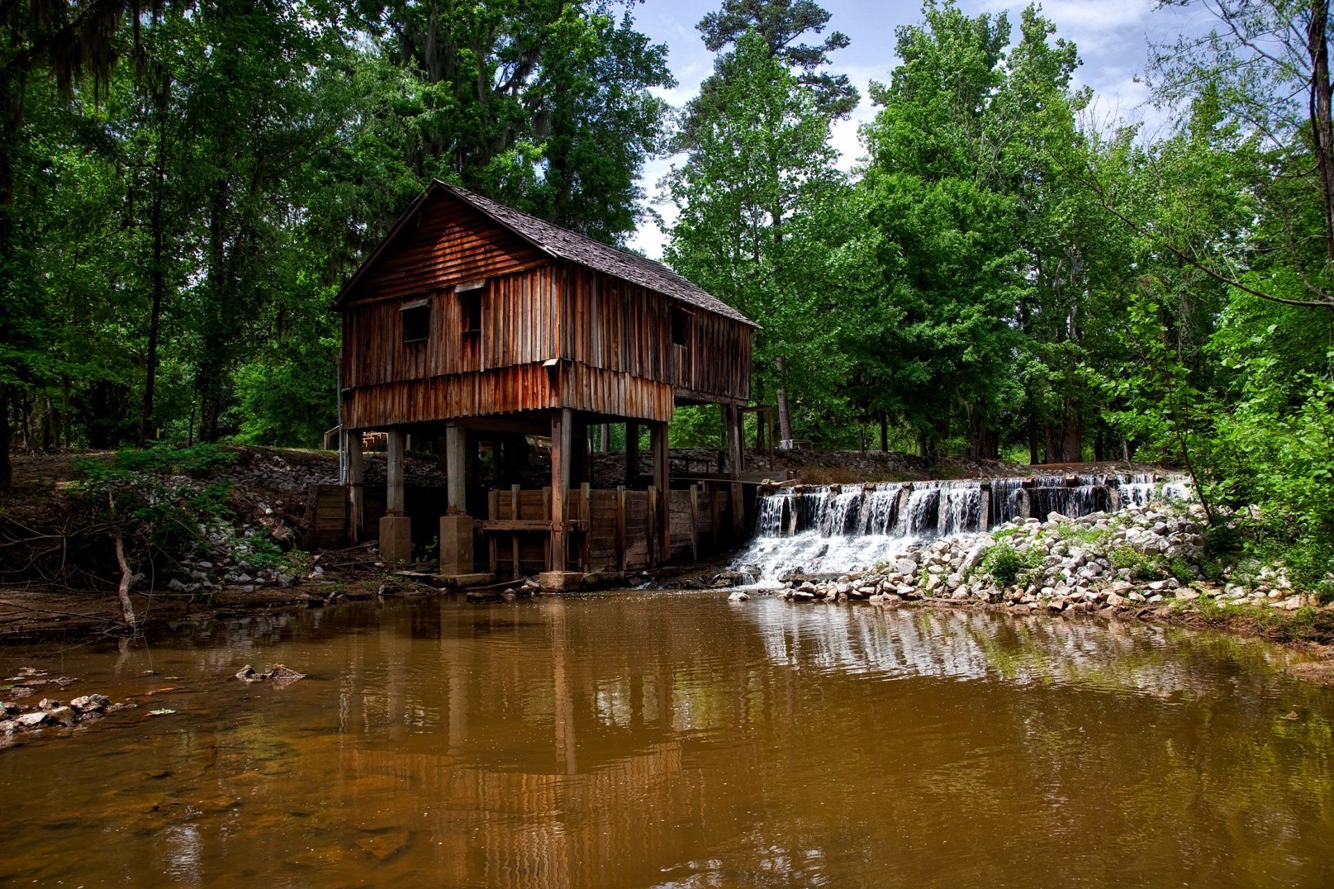 A wooden house is sitting next to a river in the middle of a forest.