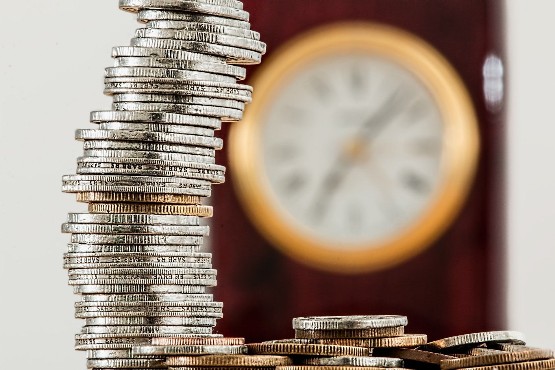 Stack of coins with a wall clock in the background