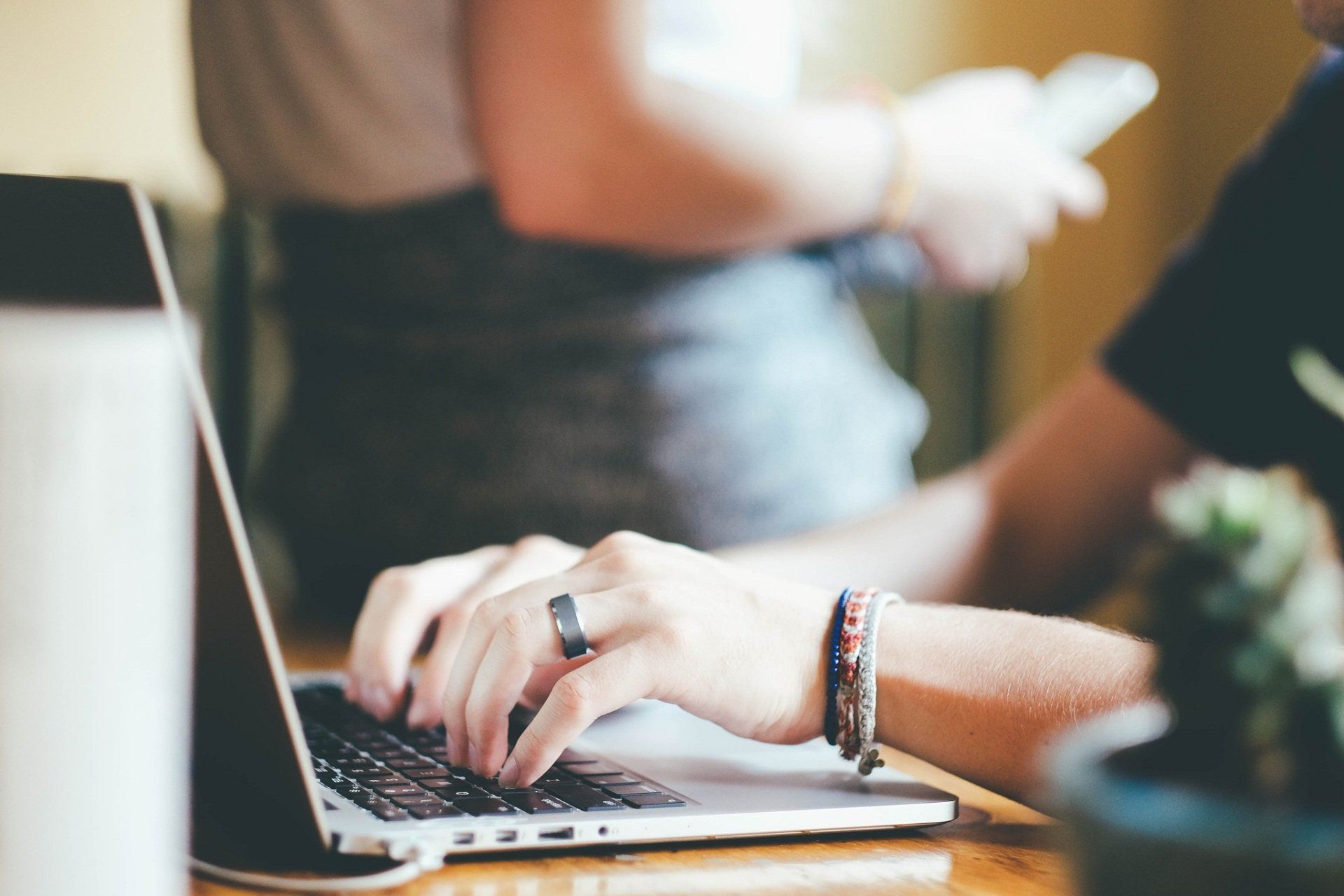 A woman is typing on a laptop with a ring on her finger.