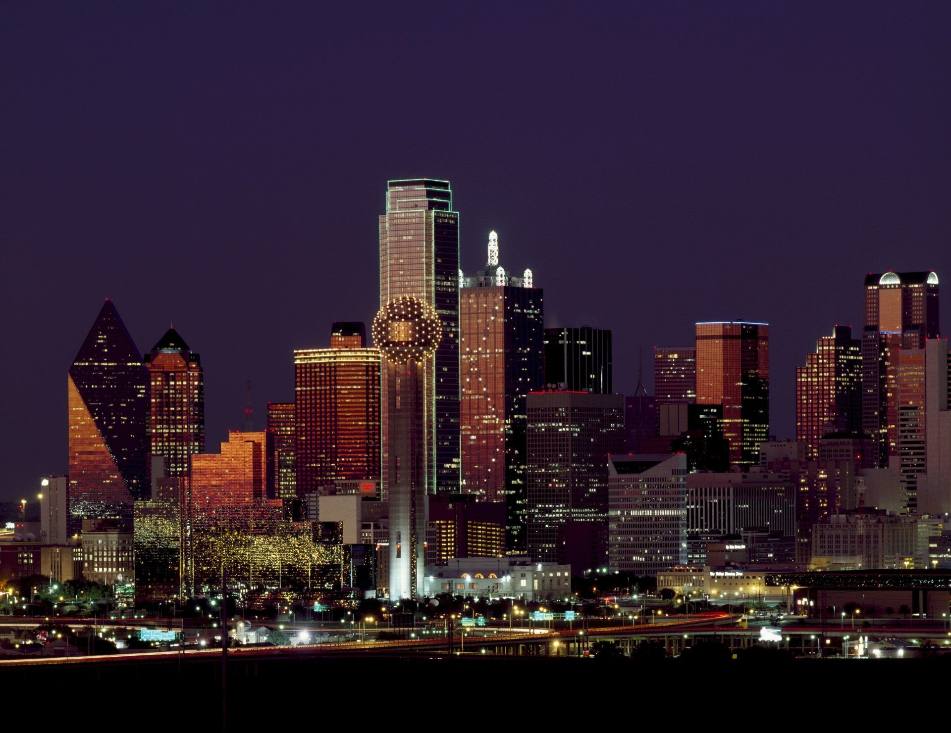 A city skyline at night with a purple sky in the background