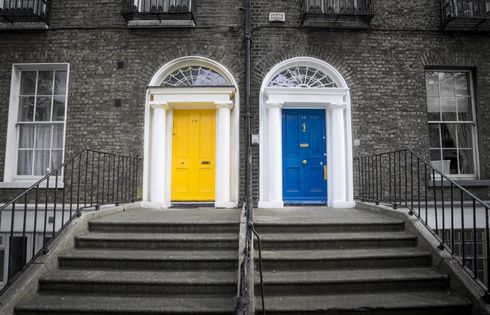 A black and white photo of two buildings with yellow and blue doors.