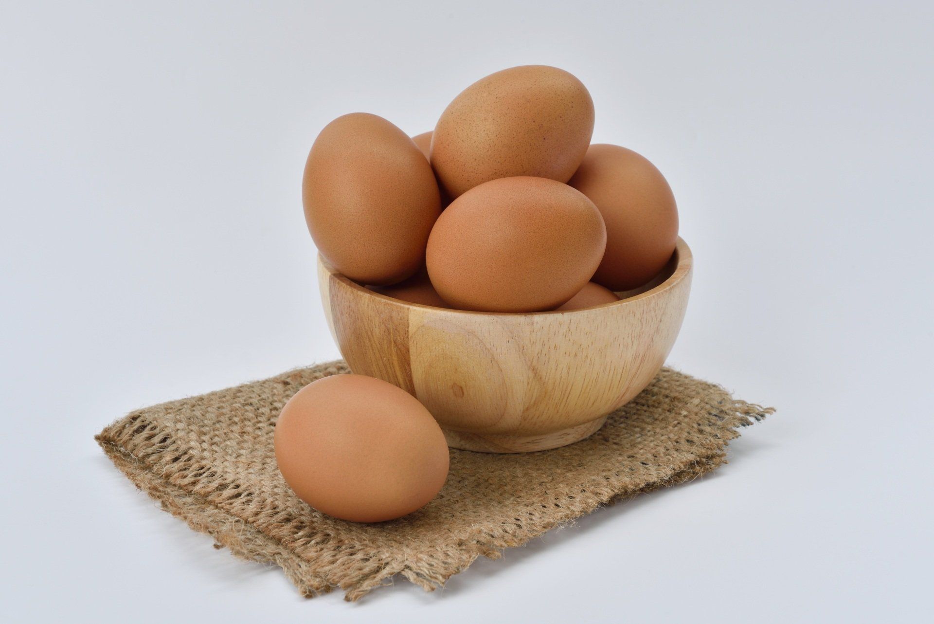 a wooden bowl filled with brown eggs on a piece of burlap .
