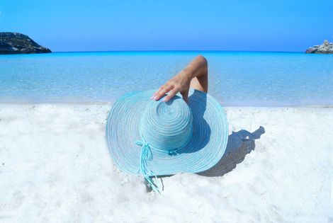 A woman is laying on the beach holding a blue hat.