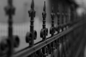 A black and white photo of a wrought iron fence railing