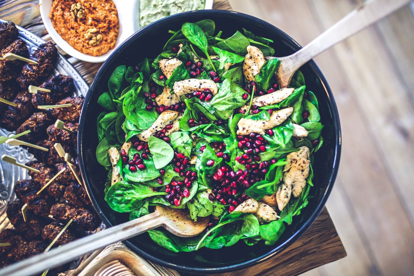 a bowl of salad with spinach , chicken , pomegranate seeds and a fork on a table .