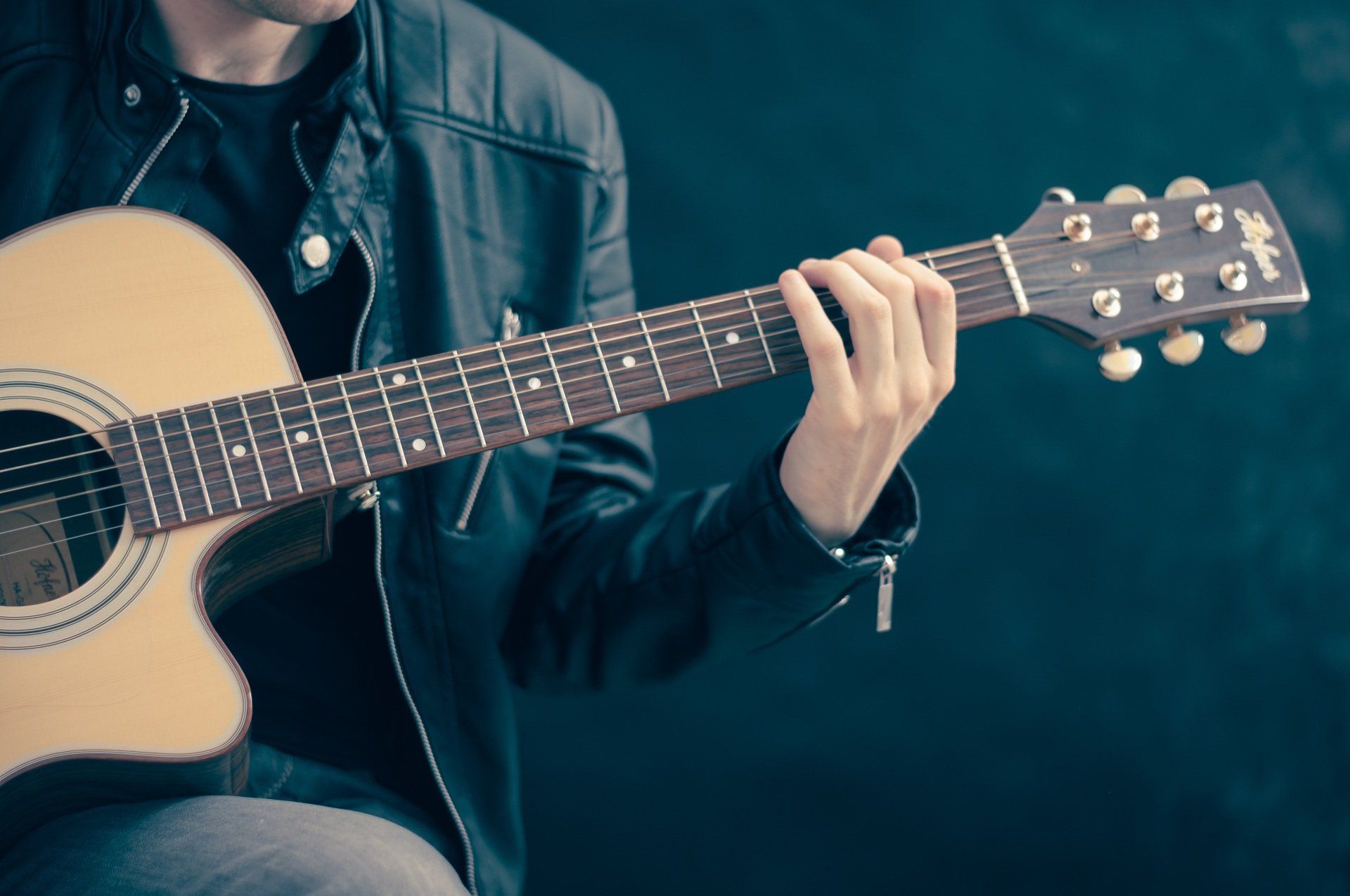 A man in a leather jacket is playing an acoustic guitar.