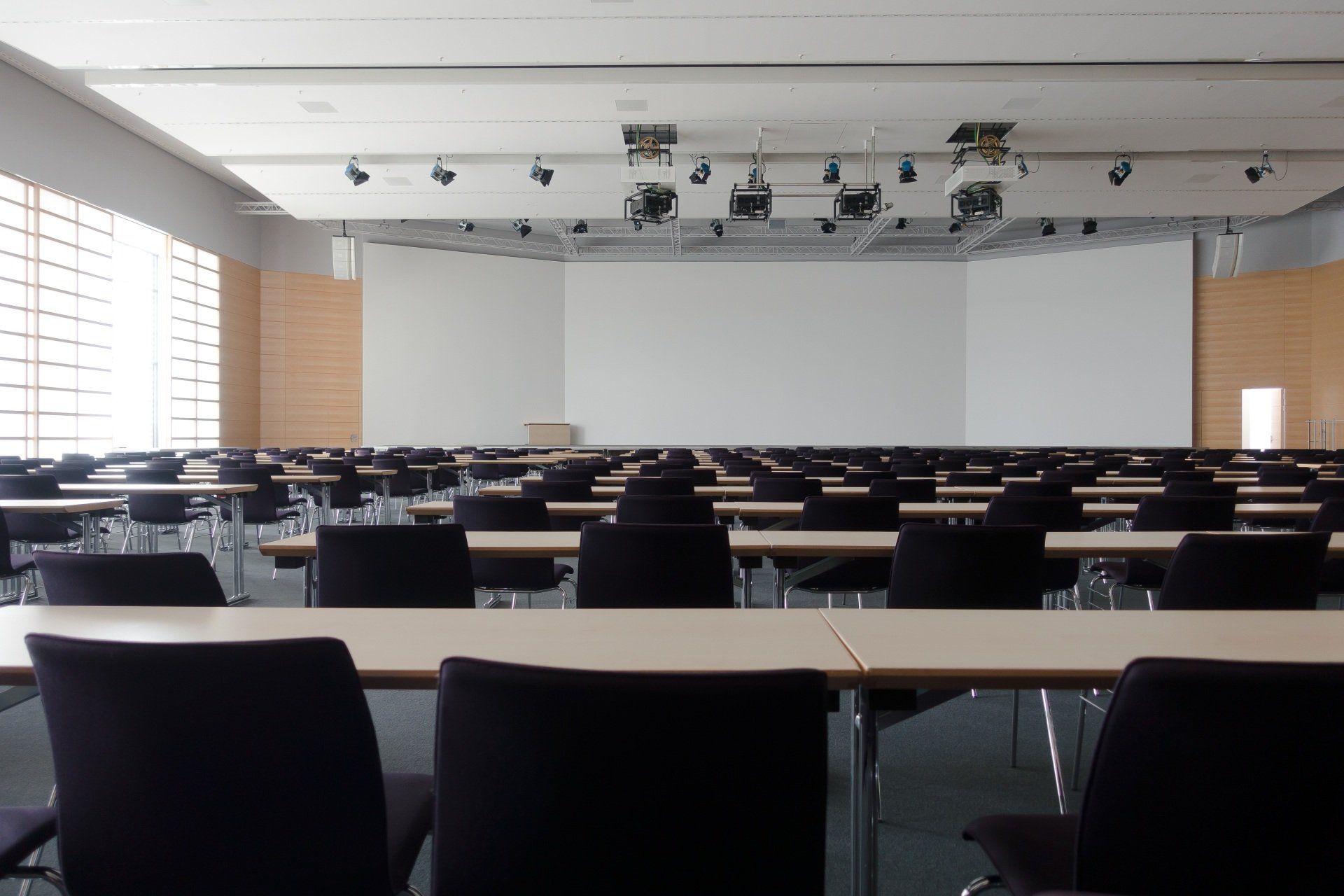An empty classroom with tables and chairs and a large screen.