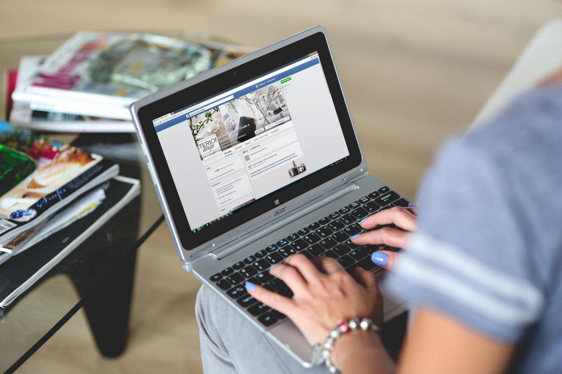 A woman is typing on a laptop computer while sitting on a couch.