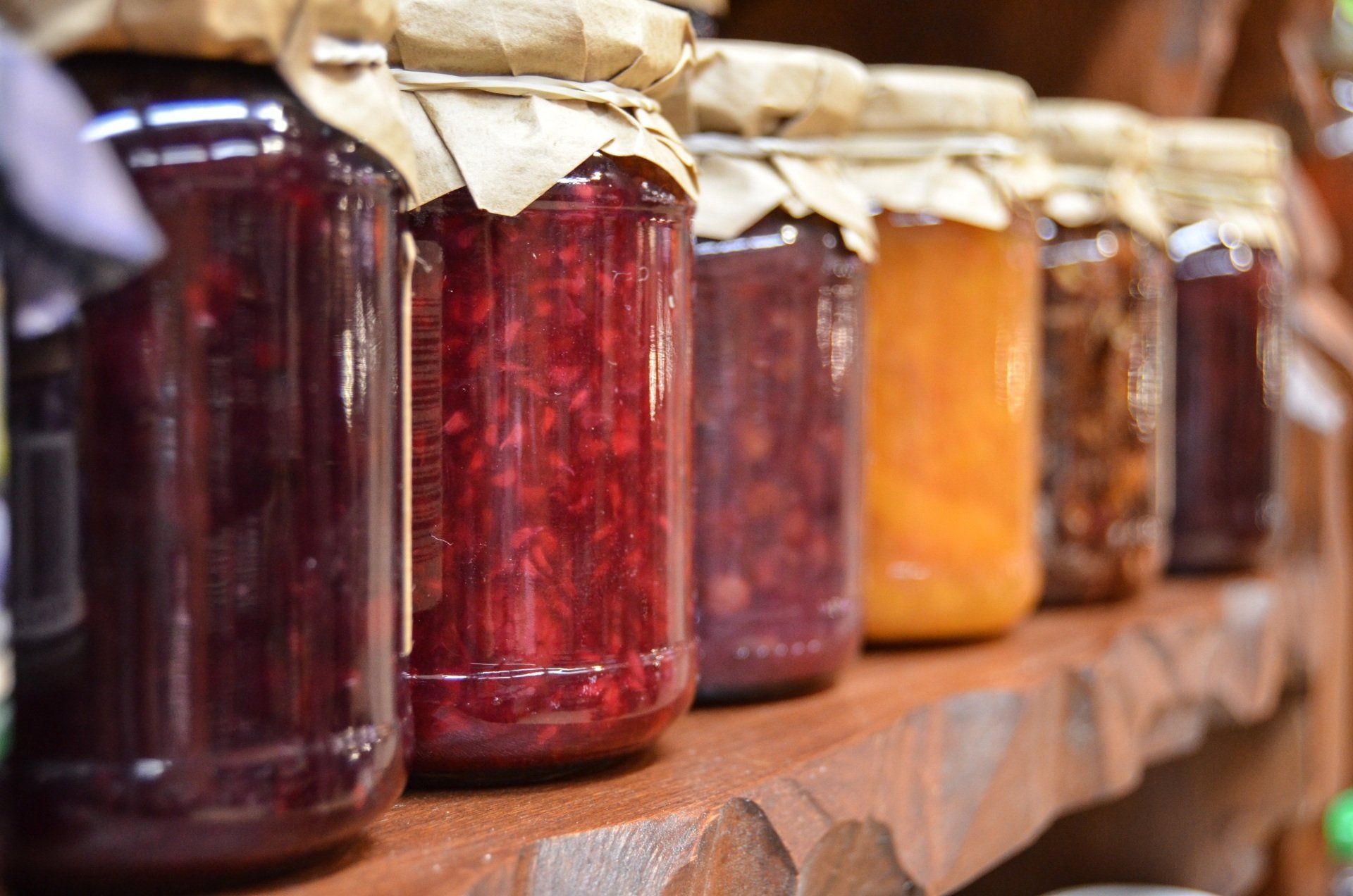 A row of jars of jam are lined up on a wooden shelf.