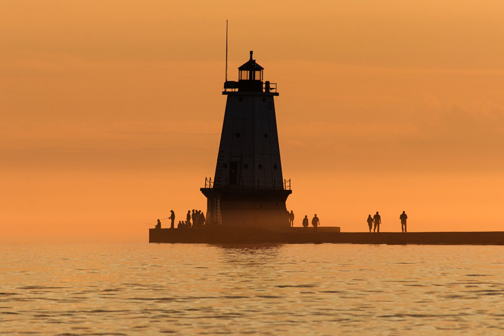 A lighthouse is in the middle of the ocean at sunset.