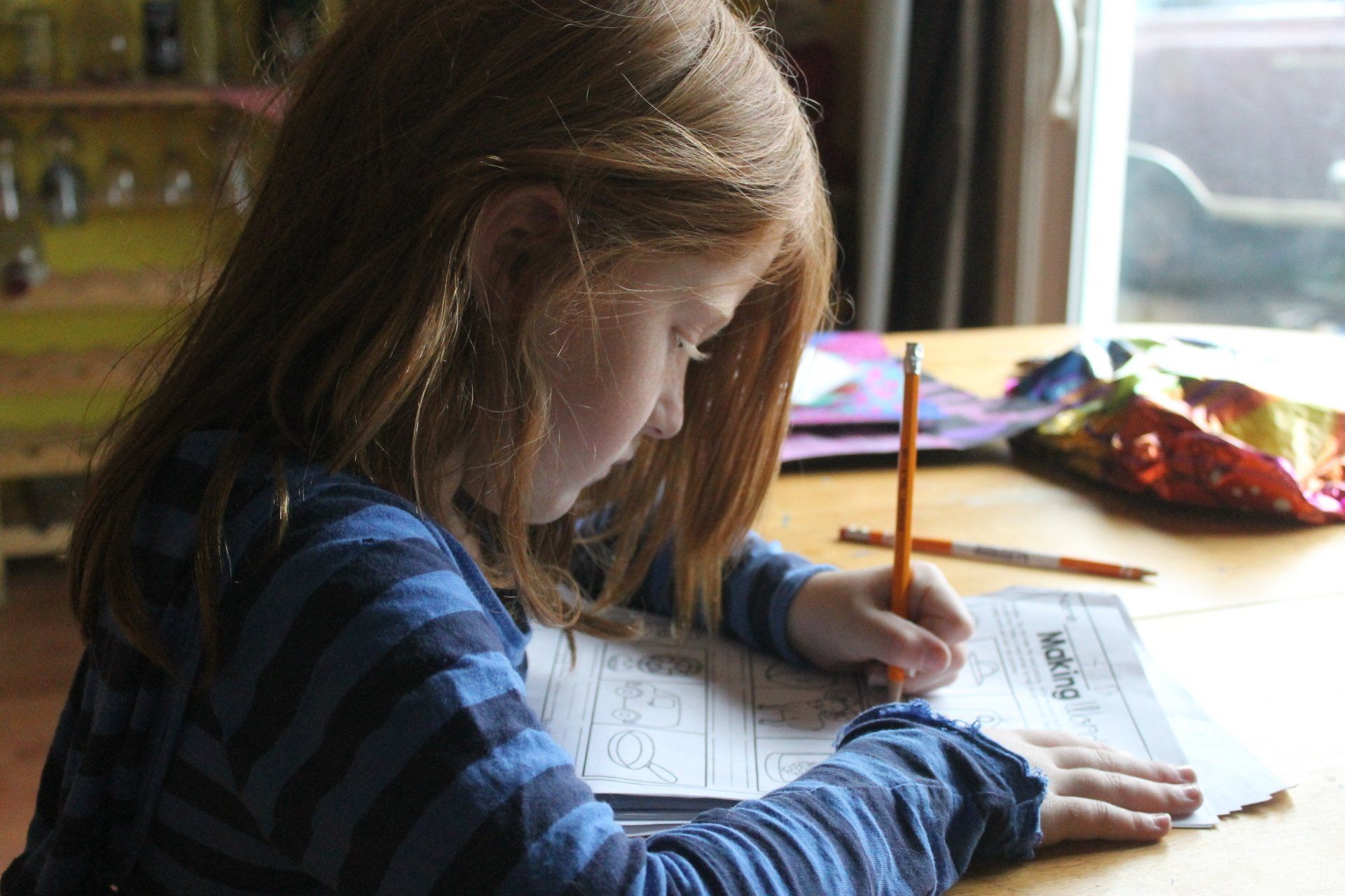 A young girl is sitting at a table writing on a piece of paper with a pencil.