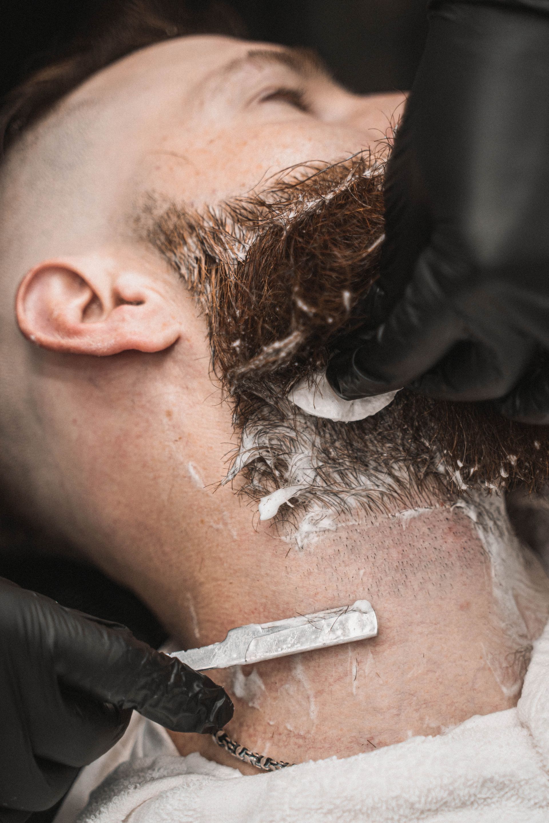 A man is getting his beard shaved by a barber with a razor.