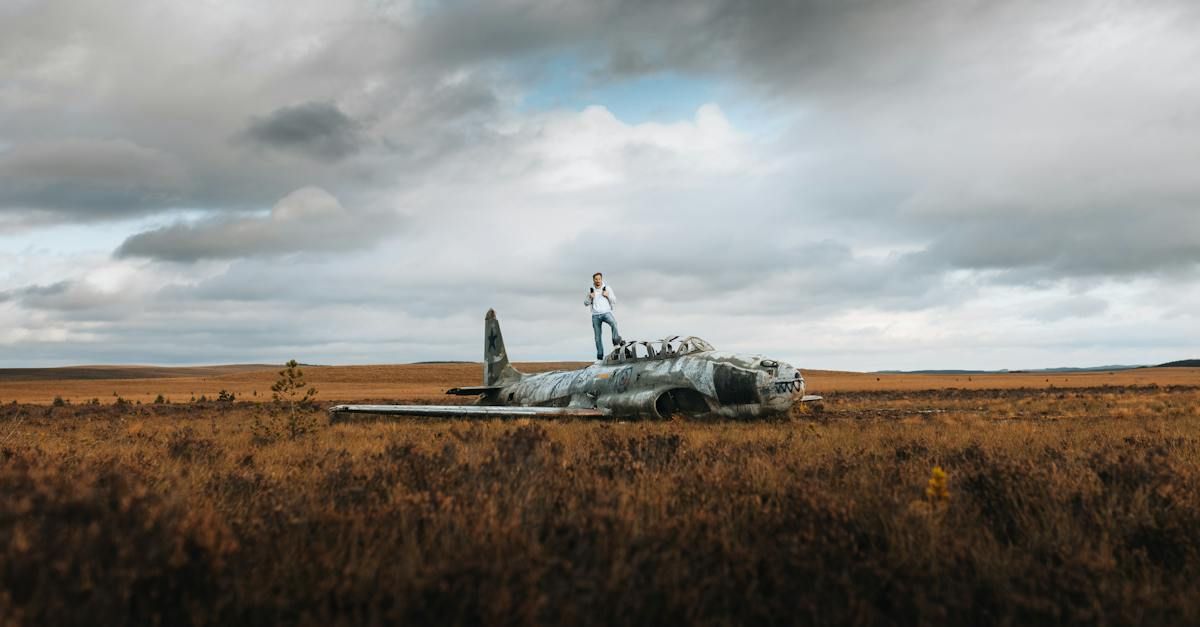 A man is standing on top of an old plane in a field.