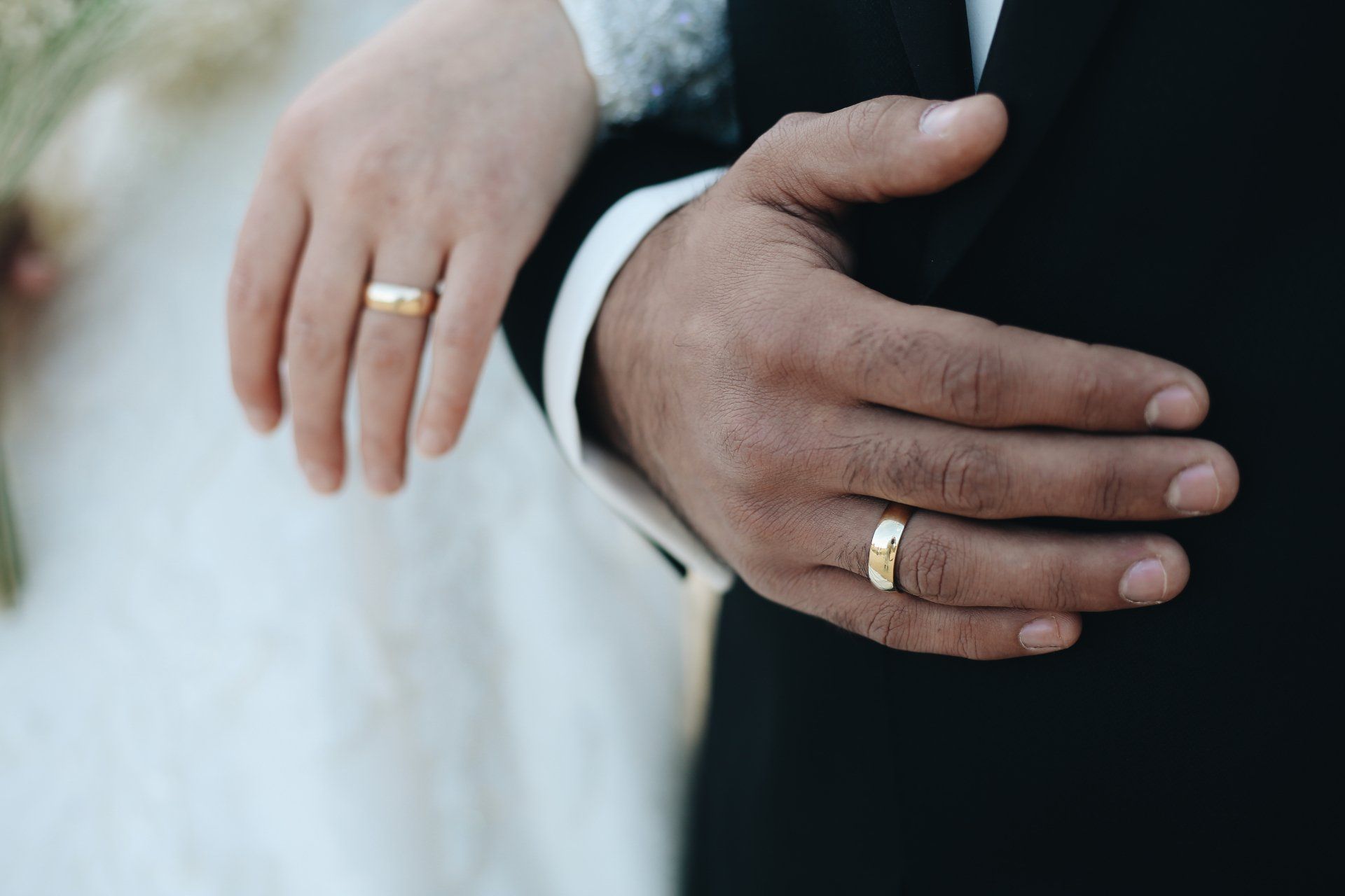 Wedding rings on the hands of a couple; one hand is light-skinned, the other is dark-skinned, both wearing gold bands.