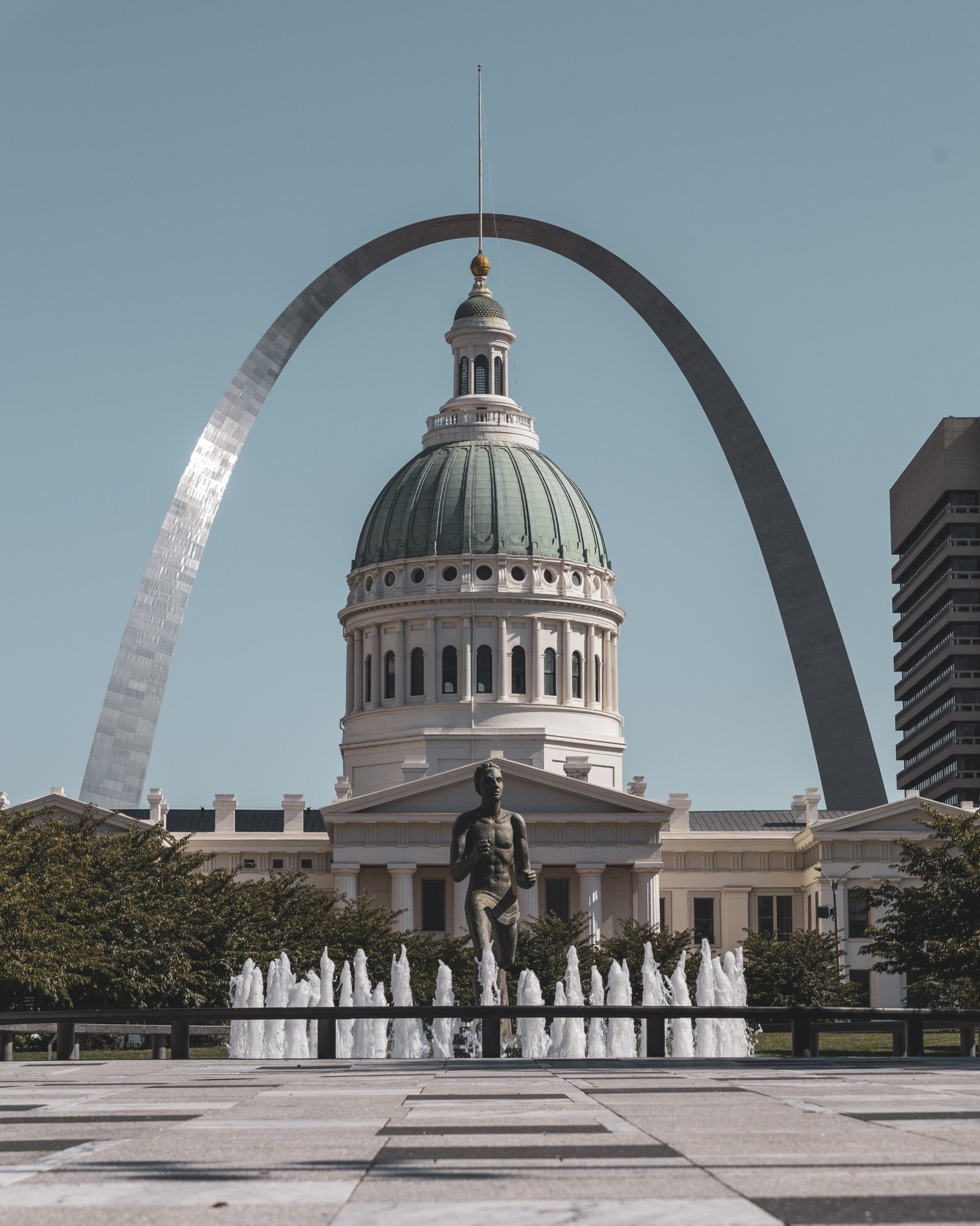 A statue of a man stands in front of the st. louis arch