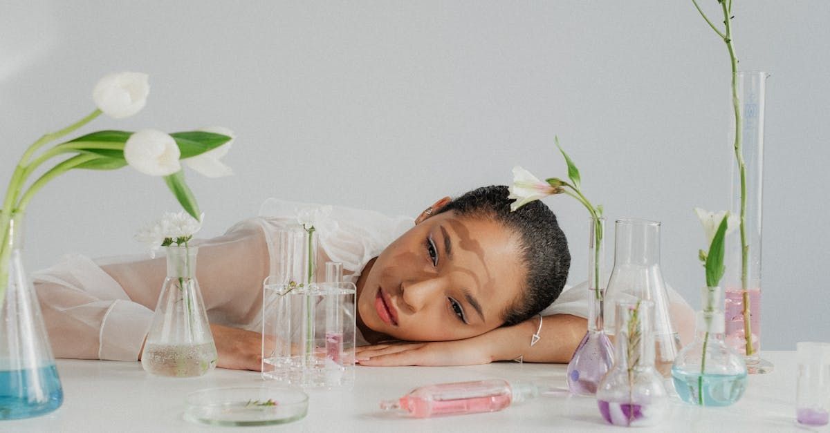 Woman resting on a white table with laboratory glassware and flowers, looking at the camera.