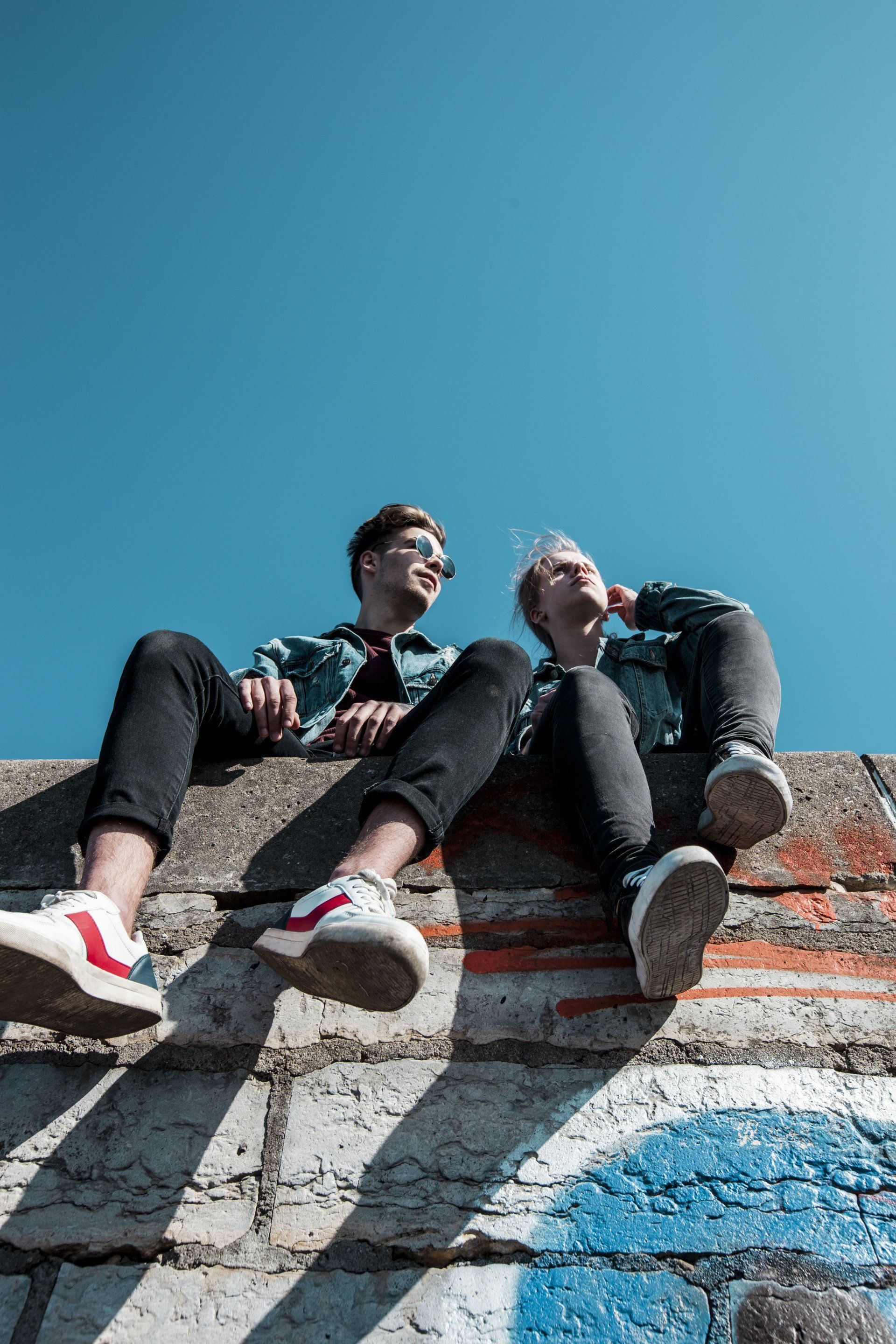 Two people are sitting on top of a brick wall.