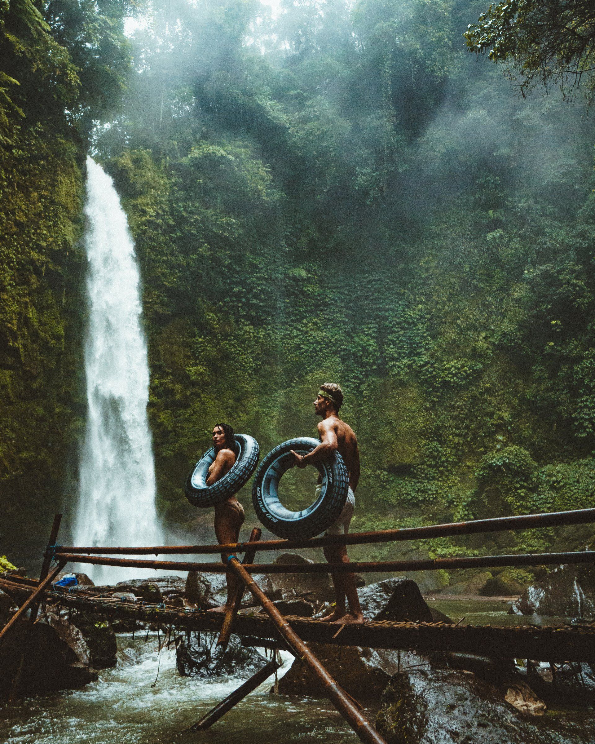 A man and a woman are standing on a bridge in front of a waterfall.