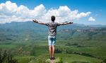 A man is standing on top of a mountain with his arms outstretched.